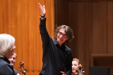 mężczyzna w okularach wskazujący ręką na solistów z uśmiechem na twarzy