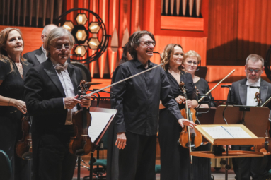 zdjęcie muzyków orkiestry i dyrygenta stojących i uśmiechających się do publiczności