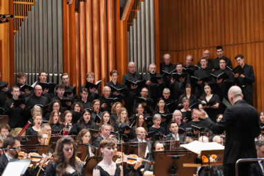 zdjęcie chóru w czarnych strojach śpiewających z nut