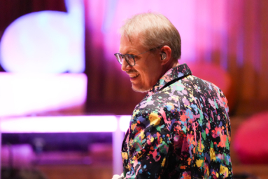 mężczyzna w okularach i kolorowym garniturze uśmiechający się do kogos