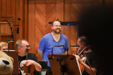 młody mężczyzna ze śmieszną fryzurą, w fioletowej koszulce, kłaniający się publiczności z rękami założonymi z tyłu