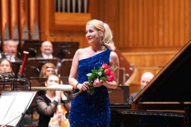 zdjęcie kobiety w cekinowej, niebieskiej sukience z odkrytymi ramionami, w ręku trzymającej róże