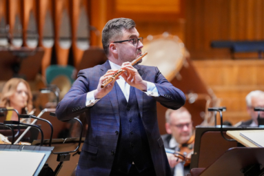 mężczyzna w eleganckim, granatowym garniturze grający koncert na flecie poprzecznym