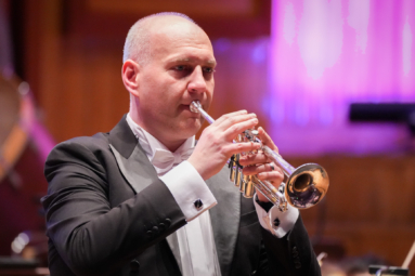 łysy mężczyzna we fraku grający na trąbce