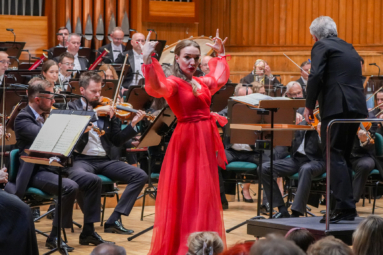 kobieta w czerwonej sukni z uniesionymi rękami jak do flamenco, śpiewająca koncert na estradzie FP