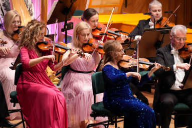 Skrzypaczki orkiestry symfonicznej FP w wieczorowych, kolorowych sukniach i skrzypkowie we frakach