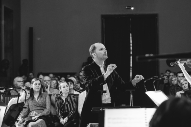 młody, łysy dyrygent skupiony na muzyce