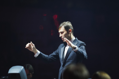 zdjęcie dyrygenta z uniesionymi rękami skupionego na utworze