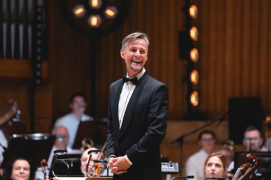 zdjęcie dyrygenta w eleganckim smokingu szeroko uśmiechającego się do publiczności