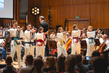 zdjęcie młodych wokalistów w strojach zespołu ABBA, którzy wyciągają przed siebie jedną rękę, a w drugiej trzymają mikrofon