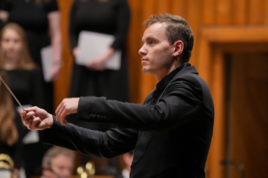 młody dyrygent w krótkich włosach i czarnym garniturze, dyrygujący orkiestrą