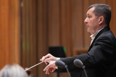 zdjęcie dyrygenta, przedstawiające jego lewy profil, trzymającego w ręku batutę