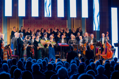 orkiestra i chór stoją na estradzie zwróceni w stronę publiczności